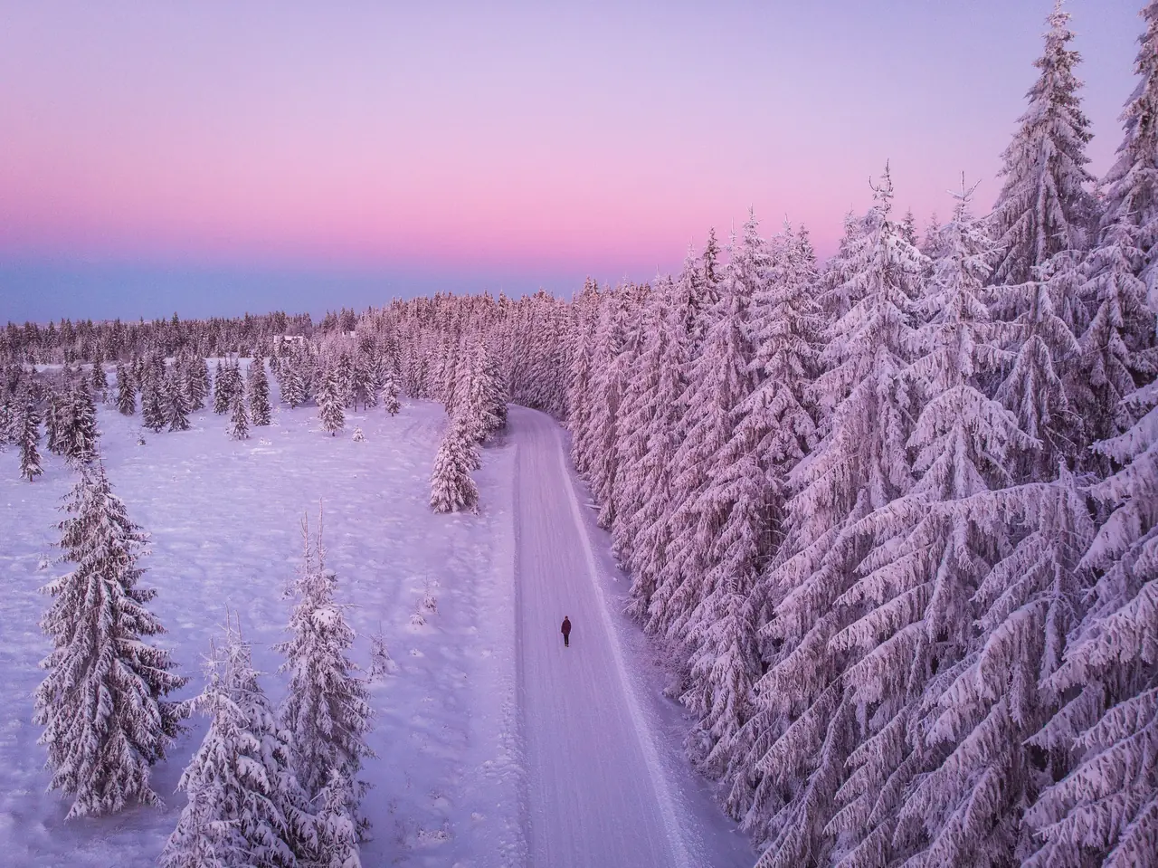 Aerial view of a snow-covered forest road at dusk with a single figure walking, for Numminen Advisory, financial leadership for startups and growing technology companies